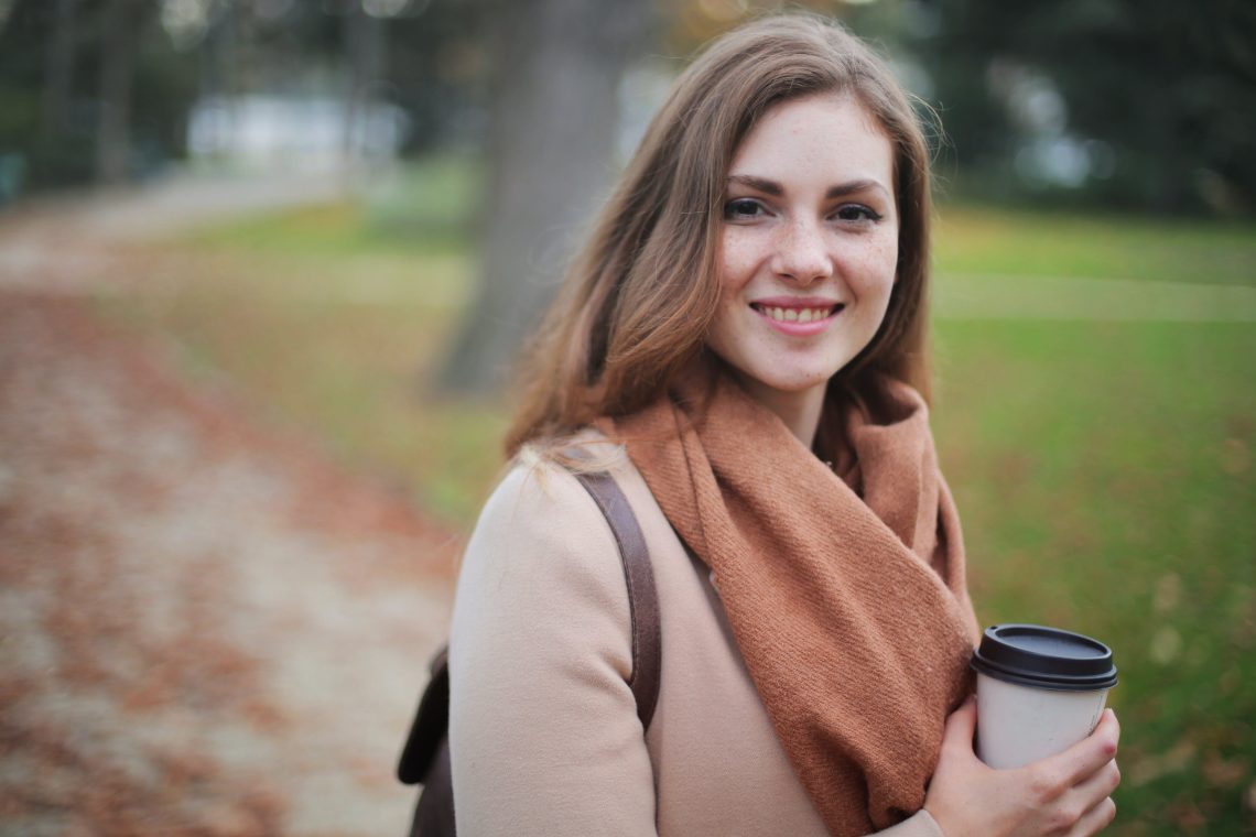 A woman drinking coffee while she can Find the perfect scarf to keep her warm.